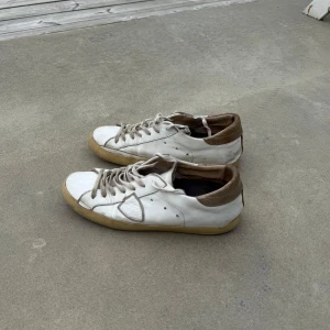 Philippe Model skor, vita - Säljer ett par vita Philippe model skor med bruna detaljer vid hälen och beige sula. Skorna har snörning och en klassisk rund tå. Perfekta för en avslappnad stil och passar till det mesta. Skriv vid frågor eller ge gärna prisförslag om ni inte vill köpa direkt😊