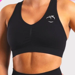 Svart sport-bh från Peach - Säljer en svart sport-bh från Peach med brottarrygg och korsade axelband. Toppen har en diskret rynkning framtill och en liten vit logga på bröstet. Perfekt för träning och ger bra stöd.
