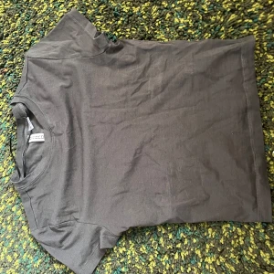 Mörkgrå t-shirt från Divided - En enkel och stilren mörkgrå t-shirt från Divided. T-shirten har rund halsringning och korta ärmar, perfekt för en clean och avslappnad look. Tillverkad i mjuk bomull för skön komfort. Tight.