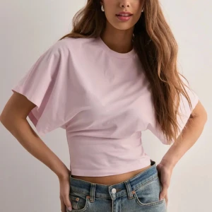Ljusrosa t-shirt med vida ärmar Nelly - Supersöt ljusrosa t-shirt från Nelly med rund hals och extra vida korta ärmar. Inte använd utan har legat i garderoben då jag inte har känt någon användning för den och är är anledningen till att den är lite skrynklig. Orginalpris: 299 