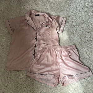 Pjamas sätt från Pretty Little Thing - Ljusrosa pjamas sätt från Pretty Little Thing, kortärmad tröja och shorts. Gjort i silke-liknande tyg.