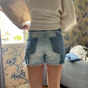 Tvåfärgade jeansshorts med rå kant - Snygga jeansshorts i två olika blå nyanser med coola kontrastpaneler och rå, fransig kant nedtill. Klassisk femficksmodell och knappgylf. Perfekta för en chill sommardag och ger en trendig vibe till din outfit.