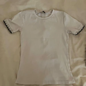 Vit t-shirt med svarta detaljer   - Vit t-shirt från Zara i bomull med korta ärmar. Ärmsluten har en unik stickad detalj i vitt och svart som ger en cool kontrast.. Perfekt för dig som gillar enkla plagg med en twist.