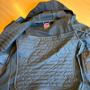 Blå quiltad jacka från Colmar - Snygg blå jacka från Colmar med quiltade partier och dragkedja framtill. Jackan har huva, två fickor med dragkedja och diskret logga på ärmen. Perfekt för att matcha med olika outfits.