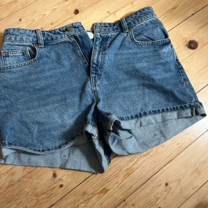 Blå jeansshorts med upprullad kant - Klassiska blå jeansshorts med upprullad kant och femficksmodell. De har hög midja och är tillverkade i robust denim. Perfekta för varma dagar och ger en avslappnad vibe. Passar dig som gillar en tidlös och enkel stil.