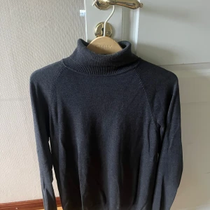 Mörkgrå polotröja från Bläck - Snygg mörkgrå polotröja från Bläck med lång ärm och klassisk ribbad krage. Perfekt att styla med jeans eller kjol för en clean look. Mjuk och skön, passar dig som gillar enkel och tidlös stil.