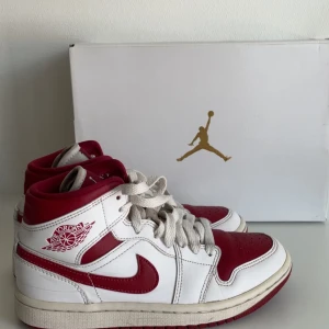 Nike Air Jordan 1 Mid röd och vit - Nike Air Jordan 1 Mid i rött och vitt. I strl 35,5 Vit bas och röda detaljer, inklusive swoosh och tåparti. Skorna har snörning och rund tå.   Nypris ca 1600
