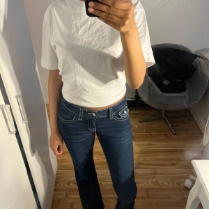 Mörkblå jeansbyxor med vita sömmar - Säljer ett par mörkblå low waist jeans, knappar och vit mönster på fickorna där bak. De är nya. OBS! Storleken är 158