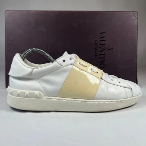 Valentino Garavani Open sneakers i vitt skinn - Jag vet inte riktigt värdet på dessa skor men Säljer ett par vita Valentino Garavani Open sneakers med en beige panel över mitten och ikoniska nitar på hälen. Skorna har snörning och rund tå, tillverkade i skinn med platt sula. Perfekta för dig som gillar stilrena och exklusiva sneakers. 