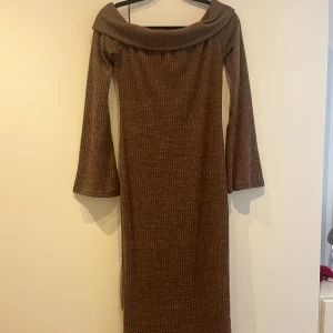 Brun ribbad offshoulder långklänning - Säljer en lång brun ribbad långklänning med offshoulder-krage och långa ärmar. Klänningen har en mjuk, stickad känsla och är perfekt för dig som gillar en stilren och bekväm look.