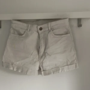Vita shorts från H&M - Säljer ett par vita shorts från H&M med klassisk femficksdesign och uppvikta benslut. Shortsen har normal passform och är tillverkade i bomull, perfekta för varma dagar.