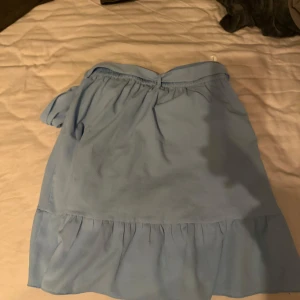 Ljusblå kjol från Vero Moda - Säljer en söt ljusblå kjol från Vero Moda. Kjolen har en omlott-design med volangdetaljer och en bekväm resår i midjan. Endast använd en gång 💙