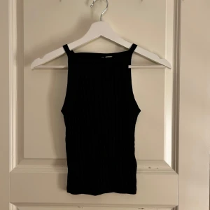 Svart ribbad linnetopp - Snygg svart ribbad linnetopp med breda axelband. Perfekt för lager-på-lager eller att bära som den är. Enkelt och stilrent plagg som passar till många olika outfits.