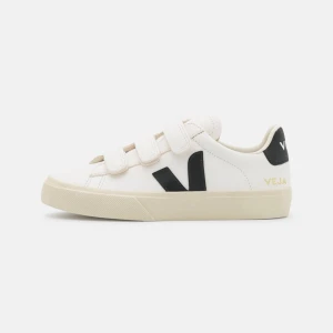 Vita sneakers med kardborreband från Veja - Snygga vita sneakers från Veja med svarta detaljer och praktiska kardborreband. Skorna har en beige sula och är perfekta för en stilren look. Veja-loggan syns tydligt på hälen