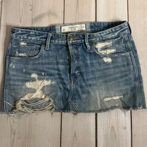 Blå jeanskjol från Abercrombie & Fitch - Snygg blå supertrendig jeanskjol från Abercrombie & Fitch med slitna detaljer och fransar. Perfekt för sommaren och våren!💕Passar perfekt på mig som vanligtvis har s💞