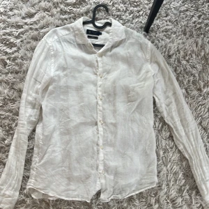 Vit linneskjorta från Riley - Säljer en stilren vit linneskjorta från Zara. Skjortan har långa ärmar och knappar framtill. Perfekt för en avslappnad men ändå elegant look. Passar bra till både jeans och chinos.