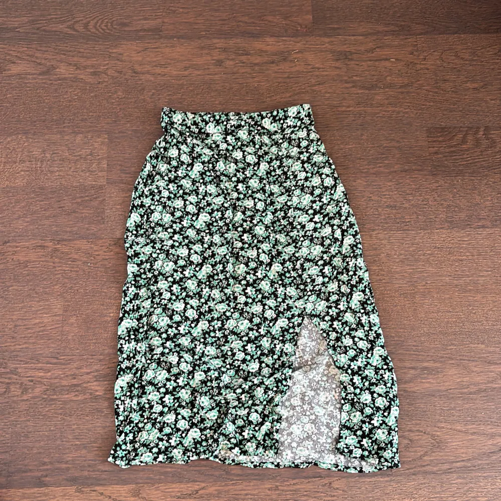 Säljer en söt blommig kjol från Lindex i grönt och svart. Kjolen har en slits på sidan och ett elastiskt midjeband för bekväm passform. Perfekt för varma dagar!❤️. Hameet.