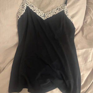 Svart linnetopp från Intimissimi - Elegant svart linnetopp från Intimissimi med vacker spetsdetalj i vitt längs urringningen. Perfekt för en stilren och sofistikerad look. Knappt använd, bara ca 2 gånger. Jättefint skick! Passar s-m då matrialet är stretchigt🥰