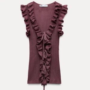 Ribbad topp från Zara - Säljer den snygga populära ribbade vinröda topp från Zara med volangdetaljer längs ärmarna och framsidan. Toppen har en v-ringning och knytband framtill. Skriv för bild i verkligheten 