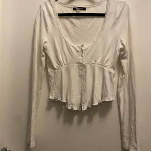 Vit långärmad topp från Gina Tricot - Säljer en söt vit långärmad topp från Gina Tricot med spetsdetaljer längs kanterna och knappar framtill. Perfekt för en stilren look. 💫 den är i helt ny skick aldrig använd 