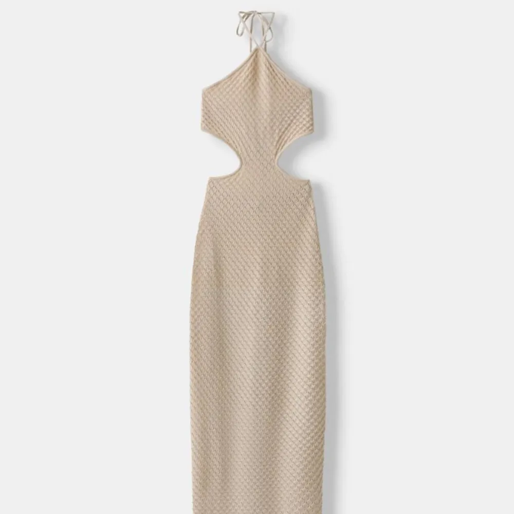 Helt oanvänd! Beige, något glittrig, klänning med stickat mönster och öppen rygg. Den har knytning i ryggen samt i nacken. Ganska liten i storleken och saknar stretch, i strl S.. Mekot.