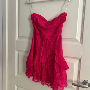 Rosa spetsklänning från Forever 21 - Snygg rosa klänning i spets från Forever 21. Axelbandslös design med volangdetaljer och knytband i midjan. Perfekt för en festlig kväll!