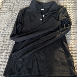 Svart ribbad långärmad tröja - Snygg svart ribbad tröja med långa ärmar och knappar framtill. Perfekt för en stilren look. Passar bra till både jeans och kjol.
