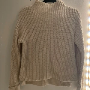 Beige stickad tröja - Säljer en mysig beige stickad tröja med hög krage. Tröjan har en ribbad struktur och långa ärmar, perfekt för kyliga dagar. Passar bra till både jeans och kjol.