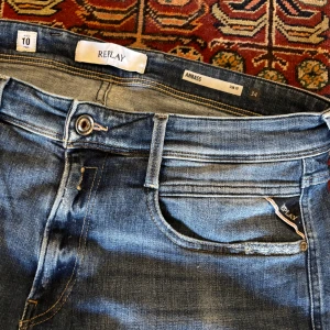 Blå jeans från Replay.OOPS!. Pris kan diskuteras! - Snygga blå jeans från Replay i modellen Anbass. De har en slim passform och är dekorerade med slitningar för en trendig look. Klassisk femficksdesign med dragkedja och knapp. Perfekta för en avslappnad stil. 