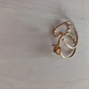 Guldfärgade ringar med stjärndetalj - Två eleganta guldfärgade ringar, en med en vriden design och den andra med en stjärnformad detalj. Perfekt för att lägga till en touch av glamour till din stil. Tror inte de är äkta guld