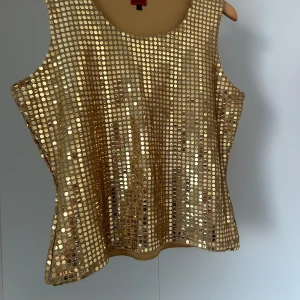 Guldglittrig ärmlös topp - Säljer en glittrig guldtop med paljetter. Den är ärmlös och perfekt för en festlig kväll. Toppen har en rund halsringning och ger en glamorös look.