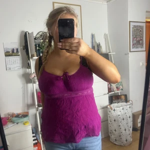 Linne - Säljer en snygg lila ärmlös topp med smala axelband och en dekorativ spetsdetalj under bysten. Toppen har en lätt rynkad textur och en liten rosett framtill. Perfekt för varma dagar!