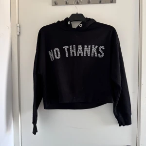Svart hoodie från FB Sister - Säljer en svart hoodie från FB Sister med texten 'NO THANKS' i glittriga bokstäver på framsidan. Tröjan har en luva och långa ärmar, samt croppad (katt o kanin finns i hemmet)