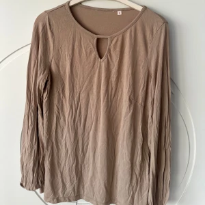 Beige långärmad topp  - Säljer en stilren beige långärmad topp. Toppen har en rund halsringning med en liten öppning framtill som ger en fin detalj. Perfekt för en avslappnad look. Passar bra till jeans eller kjol.
