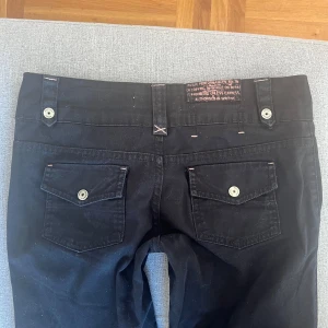 Lågmidjade jeans y2k - Svarta lågmidjade bootcut jeans med rosa detaljer och assöta fickor💕Jeansen är vintage! bershka och köpta second hand för några år sedan. Midjemåttet är 40 cm och innerbenslängden är 80cm! Skriv för mer bilder eller frågor💐