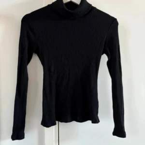 Svart ribbad polotröja från NLY Trend - Säljer en stilren svart ribbad polotröja från NLY Trend. Tröjan har långa ärmar och en klassisk polokrage, perfekt för kyligare dagar. Passar utmärkt till både jeans och kjol. Ett måste i garderoben för en chic look! Använd enstaka gång