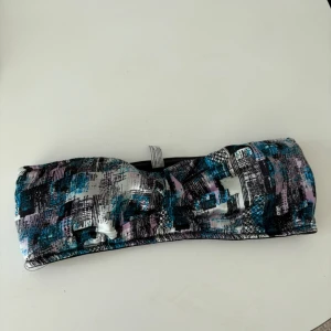 Mönstrad bandeau bikini från Lindex - Snygg bandeau bikini från Lindex i storlek M. Den har ett unikt mönster i blått, rosa, svart och vitt. Tillverkad av polyamid och elastan för en bekväm passform. Perfekt för sommarens badäventyr!