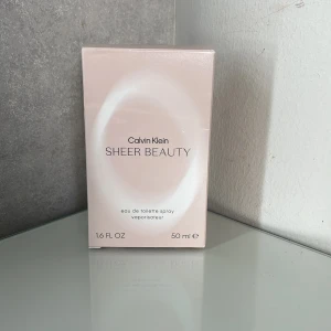 Calvin Klein Sheer Beauty Eau de Toilette 50 ml - Calvin Klein Sheer Beauty är en elegant och feminin eau de toilette i en stilren, oval glasflaska med en transparent kork. Doften kommer i en ljusrosa nyans och förpackningen är i samma mjuka ton. Perfekt för den som söker en fräsch och sofistikerad doft.+ frakt 