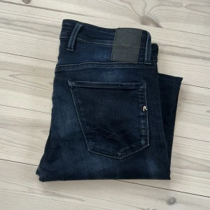 Replay anbass hyperflex - Säljes ett par replay anbass jeans med hyperflex. Dom har en diskret look med svarta sömnen och det silver polerade R:et. Storlek 29W 32L men passar även 28w. 