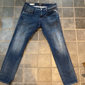 Blå jeans från Replay - Snygga blå jeans från Replay i modellen Anbass. De har en slim fit passform och är tillverkade i Hyperflex-material för extra komfort. Klassisk femficksdesign med dragkedja och knapp. Perfekta för en stilren look.