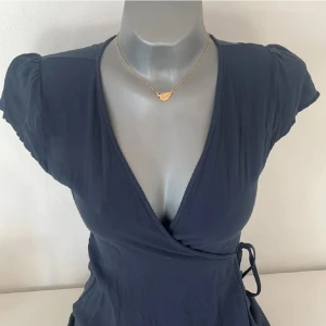 Mörkblå omlottklänning - Snygg mörkblå omlottklänning med korta ärmar och v-ringning. Klänningen har ett knytband i midjan för en smickrande passform. Perfekt för en stilren look.