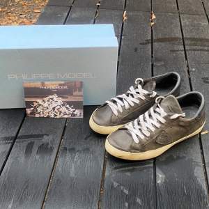 Snygga grå sneakers från Philippe Model med vit sula och vita snören. Skorna har en stilren design med en diskret logga på sidan. Perfekta för en avslappnad och trendig look. Lite slitage men inget som man tänker på 
