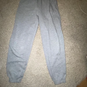 Grå mjukisbyxor från H&M - Säljer ett par grå mjukisbyxor från H&M Basics. Byxorna har en elastisk midja och muddar vid bensluten för en bekväm passform. Perfekta för en avslappnad stil. Tillverkade i en mjuk bomulls- och polyesterblandning.
