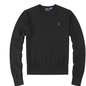 Svart tröja från Polo Ralph Lauren - Snygg svart tröja från Polo Ralph Lauren med deras ikoniska logga i rött på bröstet. Tröjan har långa ärmar och ribbade muddar vid ärmslut och nederkant. Perfekt för en stilren look.