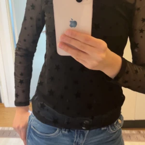 Svart mesh topp med stjärnor från Lindex - Snygg svart mesh topp från Lindex med stjärnmönster. Toppen har långa ärmar och en transparent design som ger en trendig look. Perfekt för att lägga till en touch av stil till din outfit.