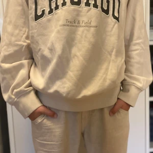 Beige sweatshirt från chicago track and Feild  - Säljer en beige sweatshirt med trycket 'CHICAGO Track & Field Illinois State Championship' på bröstet. Tröjan har en avslappnad passform, ribbade muddar och är långärmad. Perfekt för dig som gillar en clean och sportig stil.