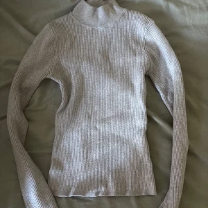 Grå ribbad polotröja från Don't Call Me Sweater - Säljer en ljusgrå ribbad polotröja från Don't Call Me Sweater i storlek S. Tröjan har lång ärm, hög krage och är i ett mjukt, stretchigt material som sitter snyggt och bekvämt. Perfekt att styla med jeans eller kjol för en clean look.