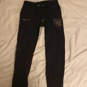 Supply & Demand mjukisbyxor - Svarta mjukisbyxor med snörning i midjan och coolt tryck på ena benet. Byxorna har muddar vid bensluten och fickor på sidorna. Perfekta för chill dagar eller när du vill ha en avslappnad stil.