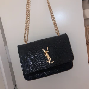 Svart YSL axelväska - Säljer en svart axelväska från YSL. Helt oanvänd. Perfekt storlek för det viktigaste och riktigt snygg detalj till din outfit. Intresserad av andra liknande väskor? Kolla in min profil
