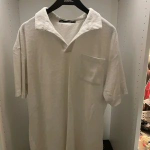 Vit frotté pikétröja  - Vit pikétröja i mjuk frotté från 157, storlek M. Tröjan har korta ärmar, klassisk krage med öppen hals och en bröstficka. Perfekt för chill sommardagar eller strandhäng. Enkel och clean look som funkar till det mesta. Aldrig använd.